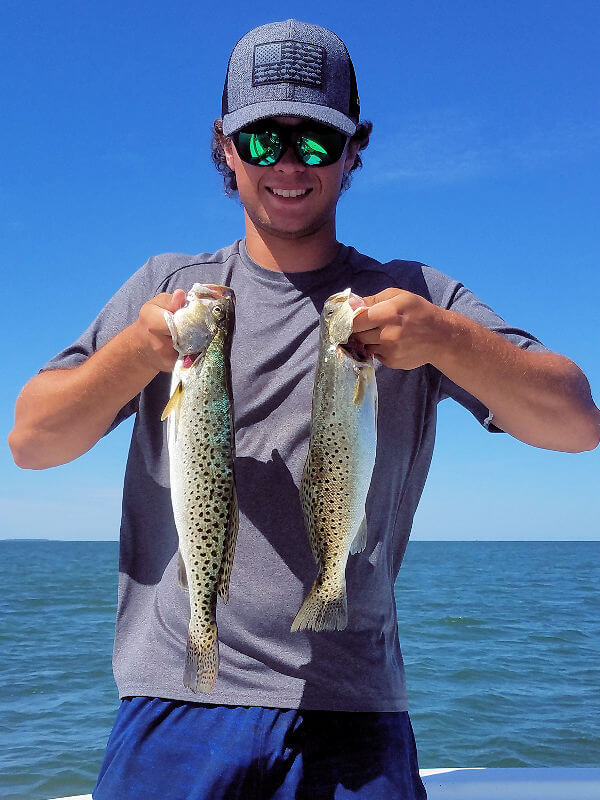 Young angler holds two Speckled Trout for the camera.